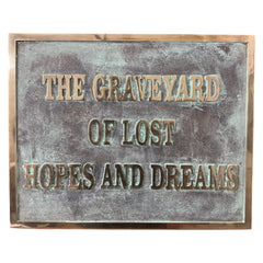Bronze plaques with text 'The Graveyard of Lost Hopes and Dreams' on a textured surface.