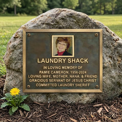 Bronze Memorial plaque for Pamie Cameron on a rock with a yellow flower in front, set against a natural background.