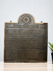 Bronze plaque with engraved text and a seal on a white background