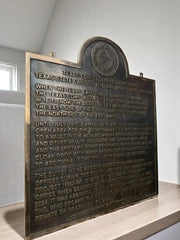 Bronze plaque with engraved text on a wooden stand against a neutral background