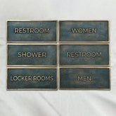 Custom antique brass door sign with raised lettering - Set of restroom signs with labels for Restroom, Women, Shower, Restroom, Locker Rooms, and Men on a white background.