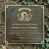 Plaque commemorating the Kensington Watermill, a National Historic Place, on a stone wall with ivy.