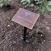 Memorial plaque for Astrid Artho in a garden setting with a small tree.