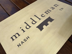 Brass sign with 'middleman' and 'NASH' text on a wooden surface