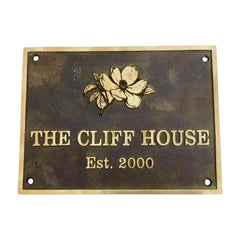 Bronze metal sign with floral design and text 'The Cliff House Est. 2000' on a white background