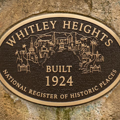 Personalized bronze memorial plaque with raised lettering with 'Whitley Heights' text and building illustrations on a stone wall.