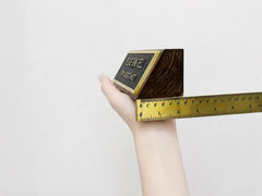 Hand holding a gold bar with a ruler for scale on a light gray background