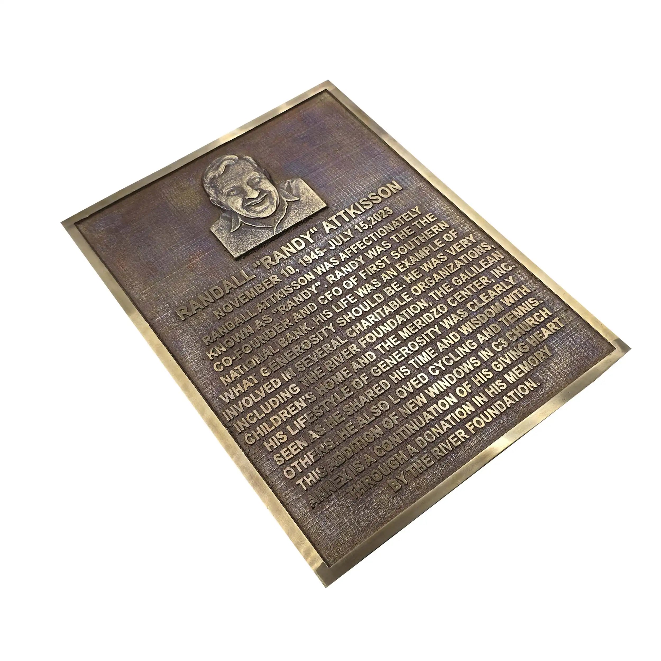 A rectangular bronze historical plaque with a raised portrait and engraved text, shown at an angle on a plain white background.