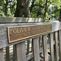 Wooden bench with a brass bench memorial plaque bearing a name and dates in a park setting
