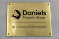 Brass plaque with Daniels Property Group logo and website on a gray background