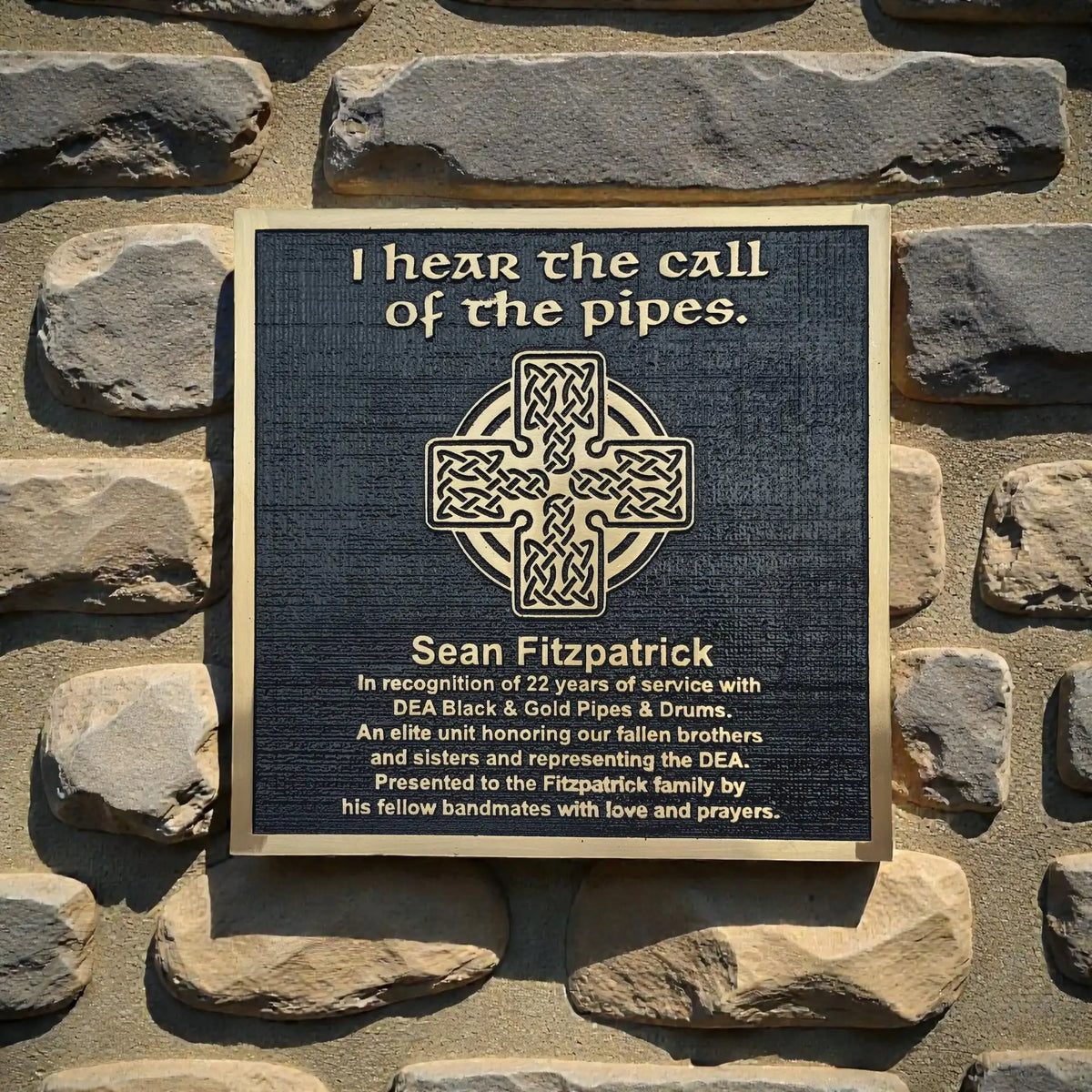 Bronze Plaque on a stone wall with text and a Celtic cross design.
