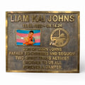 Bronze plaque with engraved text and a photo of a person, on a white background