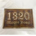 Bronze house number sign with '1320 Moore Road' on a white background