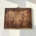 Decorative address sign for 'The Honey House' with floral and bee designs on a white wall.