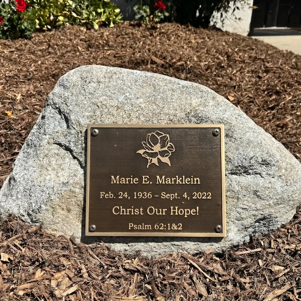 Bronze Memorial plaque on a rock with engraved text and floral design.