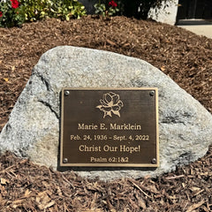 Bronze Memorial plaque on a rock with engraved text and floral design.