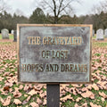 Bronze memorial sign with text 'The Graveyard of Lost Hopes and Dreams' in a cemetery.