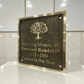 Memorial plaque with tree design and engraved text on a reflective surface.