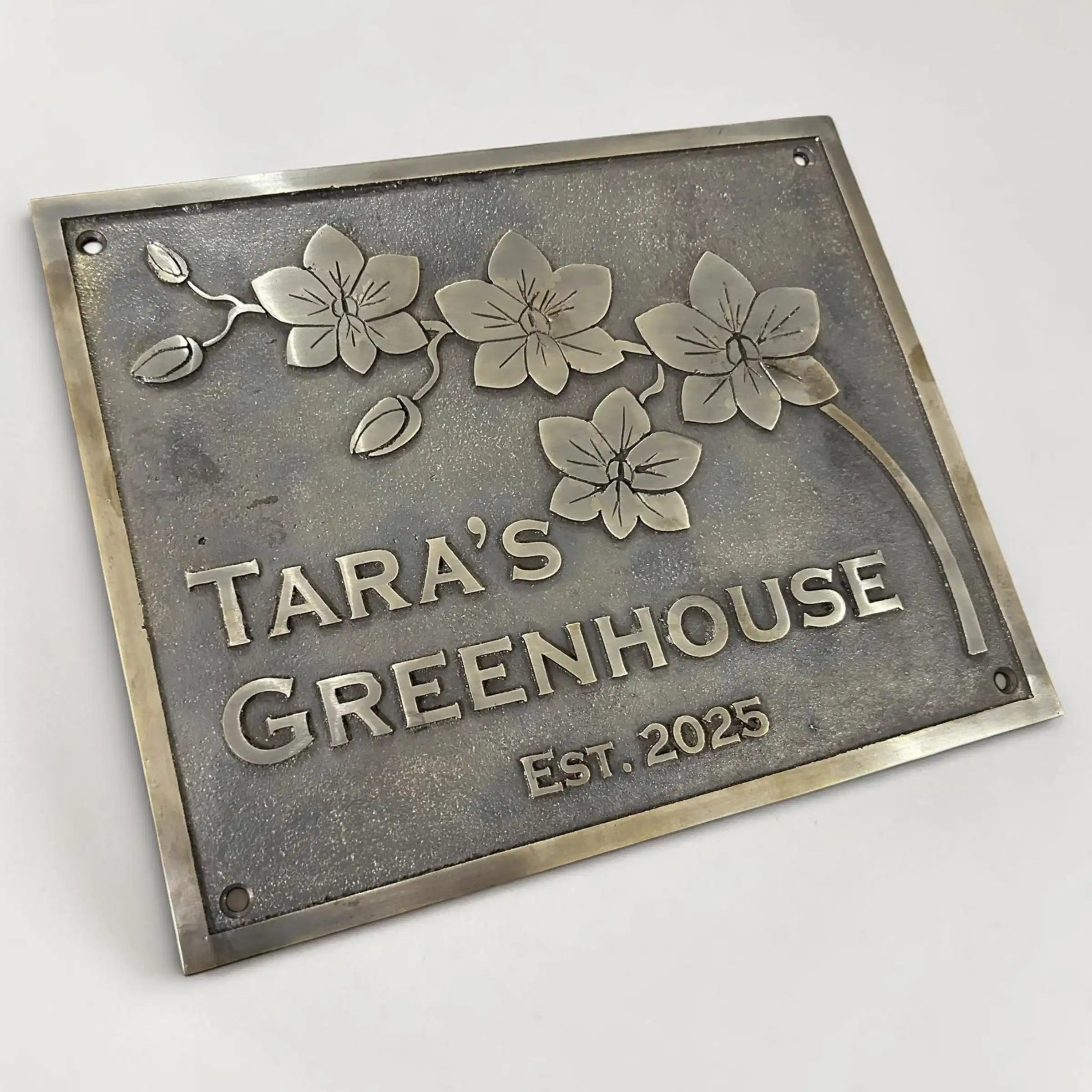Bronze metal sign with floral design and text 'Tara's Greenhouse Est. 2025' on a white background