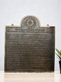 Bronze plaque with engraved text and a seal on a white background