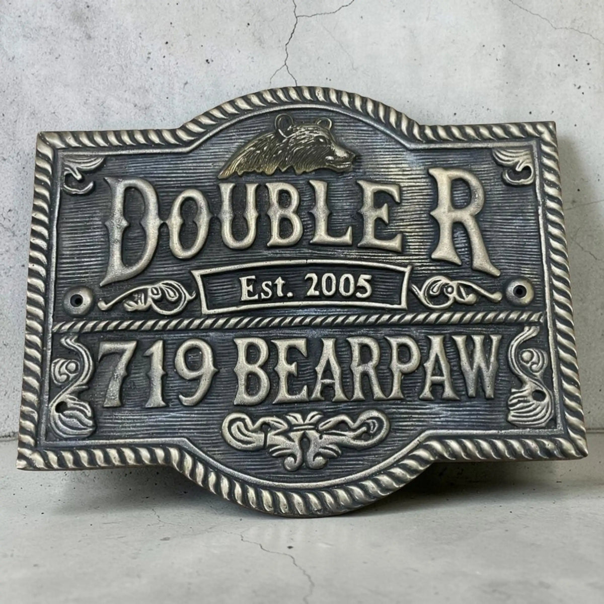 Decorative bronze sign with 'Doublerr' and '719 Bearpaw' text on a textured surface