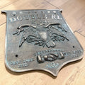 Bronze plaque with an eagle emblem and engraved text on a wooden surface