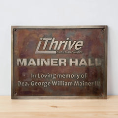 Bronze plaque with 'iThrive Christian Church' and 'Mainer Hall' text on a wooden surface.
