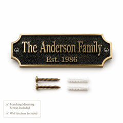Custom family nameplate plaque with a black textured background and gold lettering, shown with two gold mounting screws and two white wall anchors on a white background. A small text box at the bottom left notes that matching mounting screws and wall anchors are included.