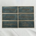 Custom antique brass door sign with raised lettering - Set of restroom signs with labels for Restroom, Women, Shower, Restroom, Locker Rooms, and Men on a white background.