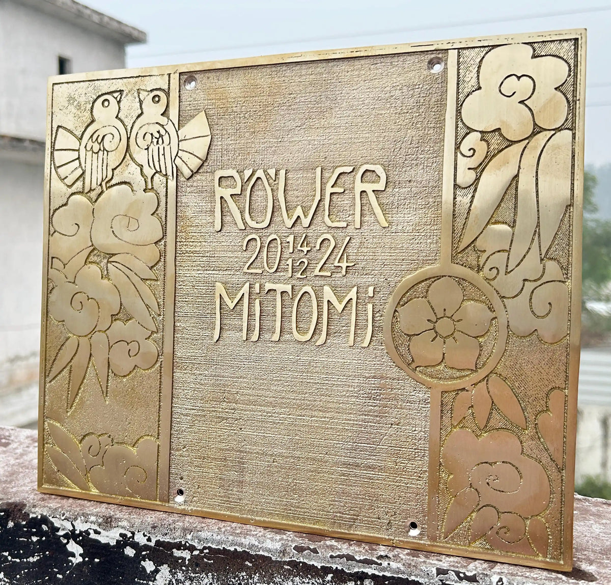 Decorative metal plaque with engraved designs and text on a wooden surface.