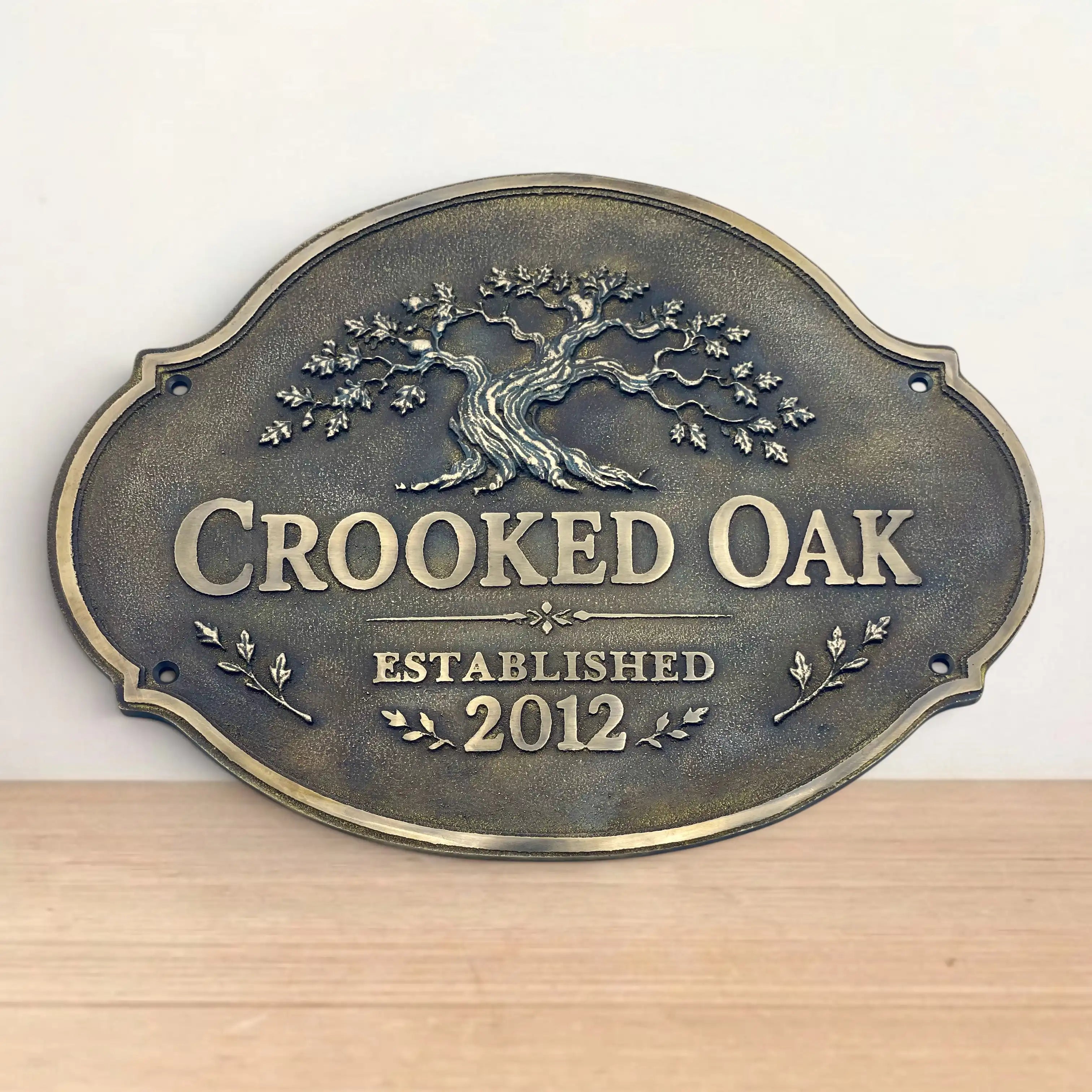 Bronze sign with 'Crooked Oak' and tree design on a wooden surface.