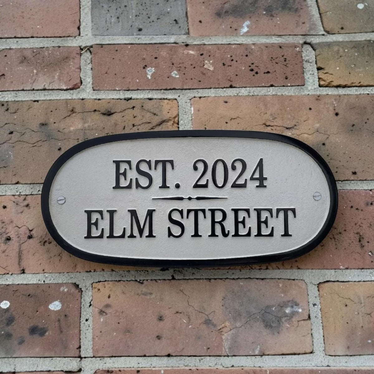 House number sign on a brick wall with 'EST. 2024 ELM STREET' text.