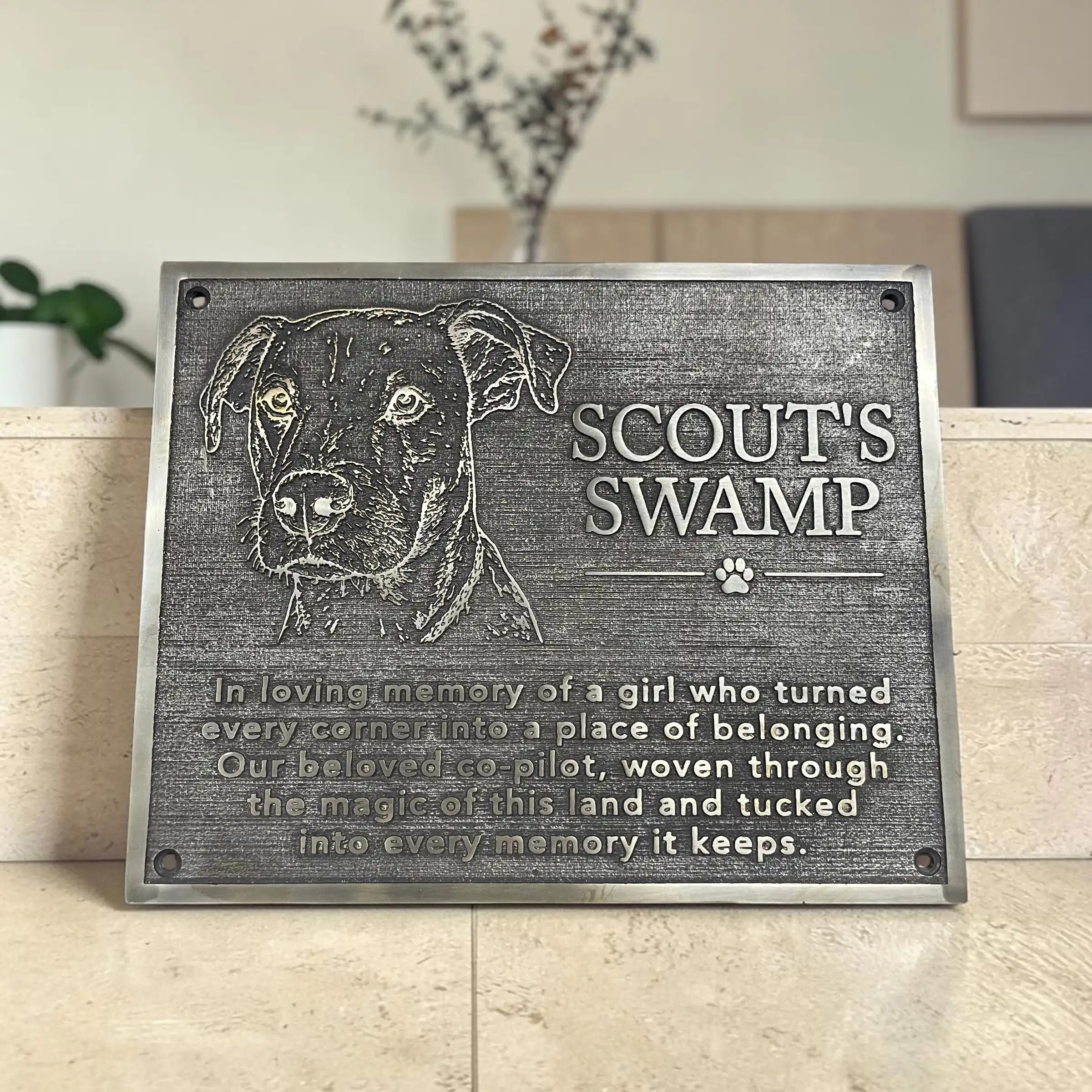 Memorial plaque for a dog named Scout's Swamp with engraved text on a wooden surface.