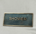 Rectangular metal sign with 'SHOWER' text on a gray background