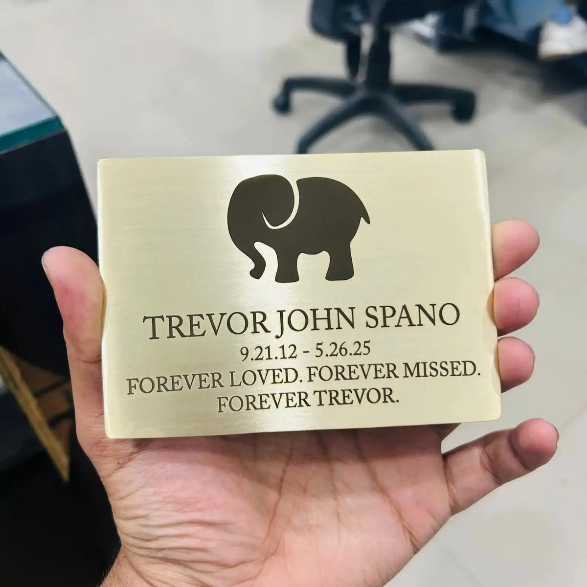 Brass Memorial plaque with elephant silhouette and text held in a hand, blurred office background