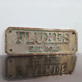Bronze plaque with 'FLUXES EST. 2022' text on a white background