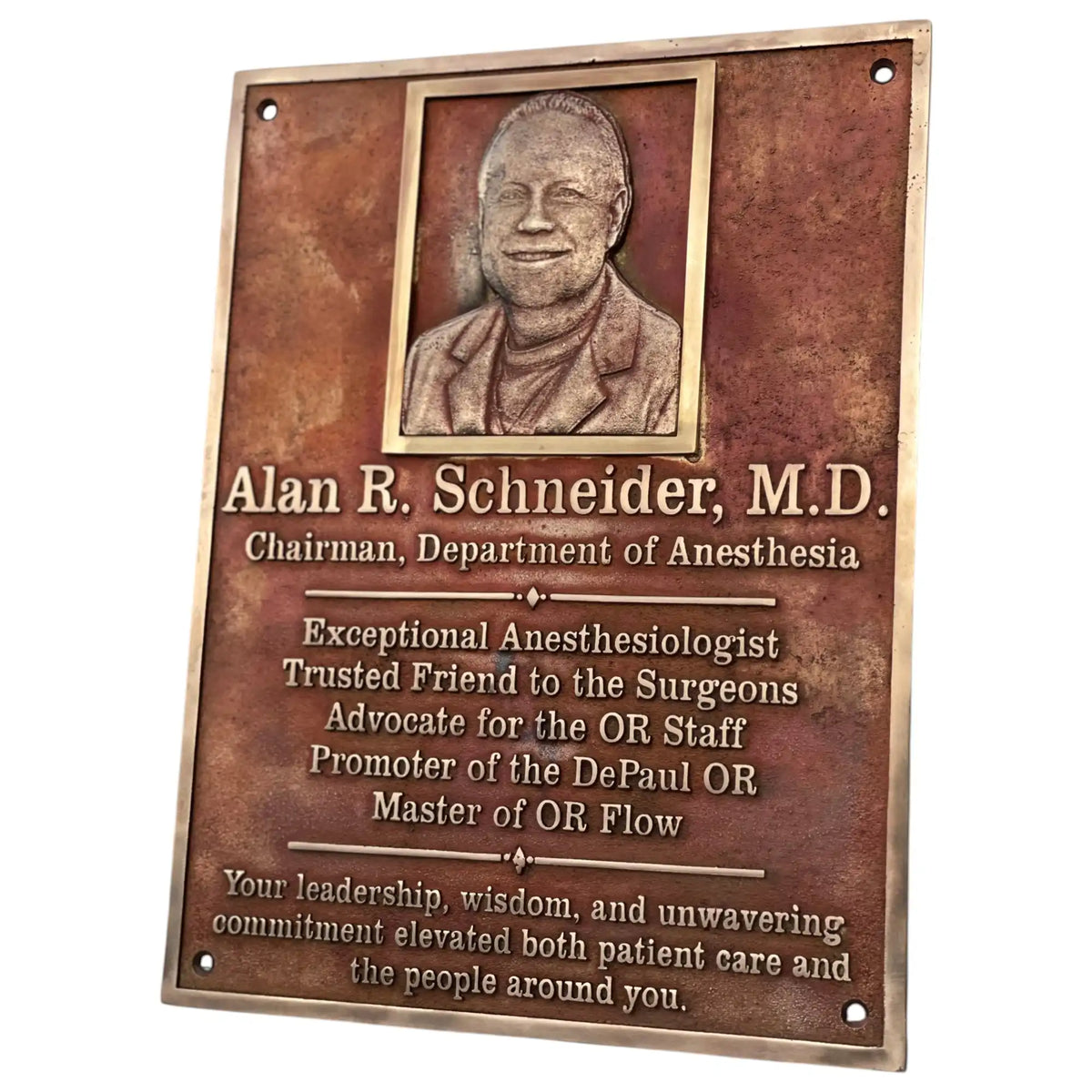 Bronze plaque with a portrait of Alan R. Schneider, M.D., and engraved text on a white background.