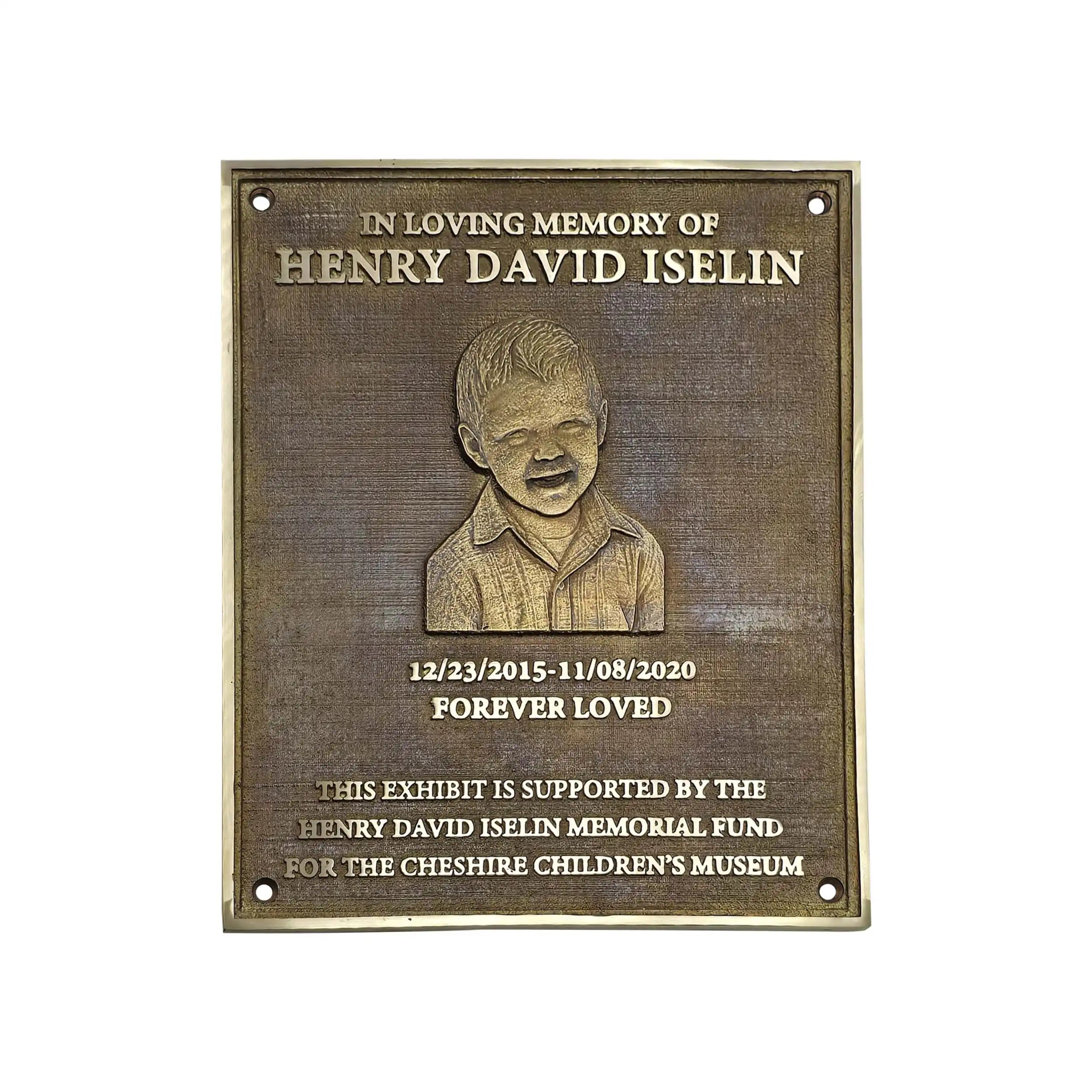 A rectangular bronze memorial plaque with rounded corners, featuring an engraved portrait of a young boy and personalized text reading 'In Loving Memory of Henry David Iselin' and 'Forever Loved,' on a plain white background.