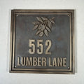 Cast bronze house number plaque - Metallic house number sign with '552 LUMBER LANE' on a textured wall.
