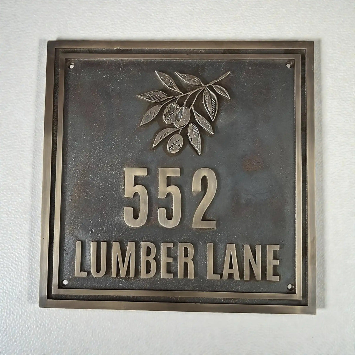 Cast bronze house number plaque - Metallic house number sign with '552 LUMBER LANE' on a textured wall.