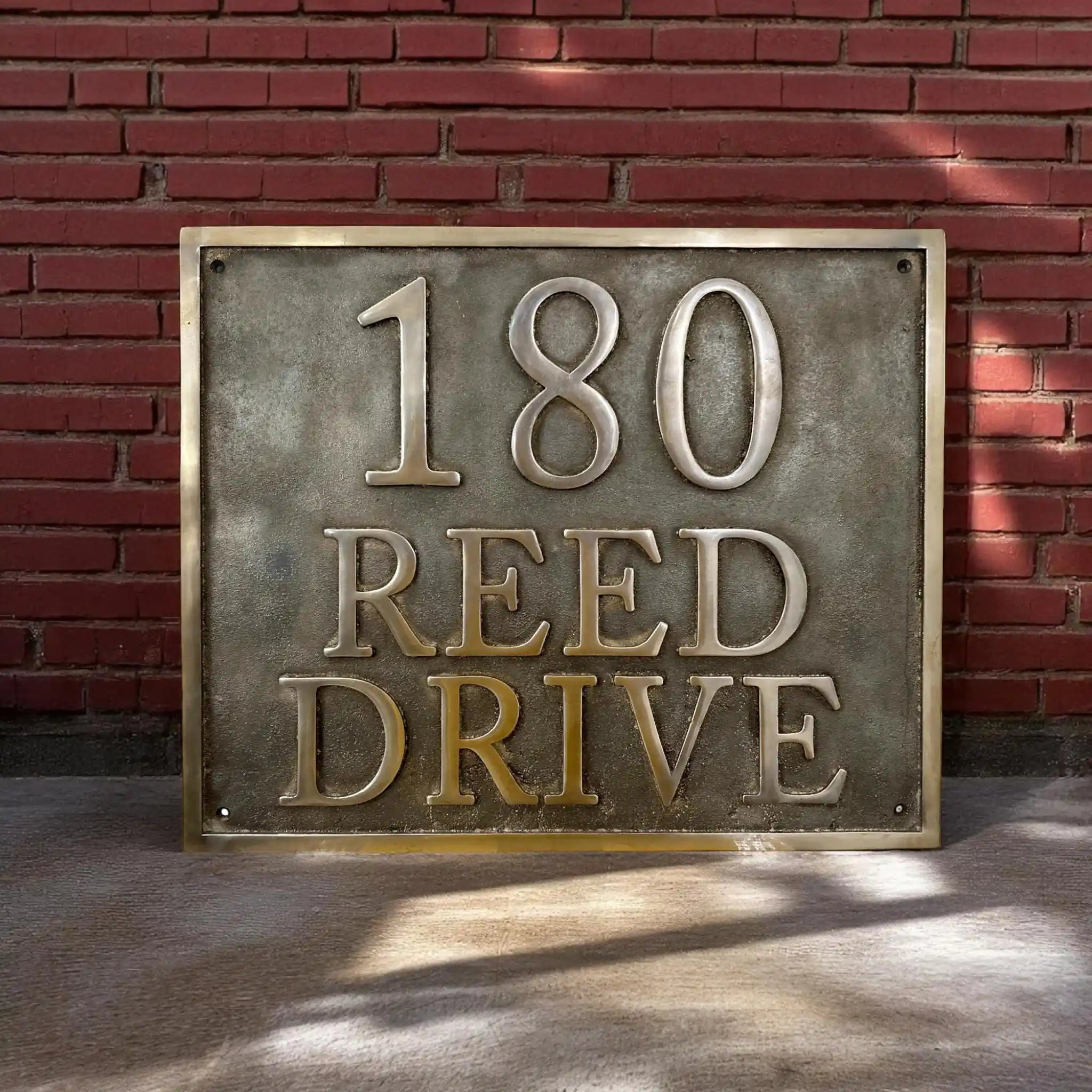 Bronze address sign reading '180 REED DRIVE' against a brick wall.
