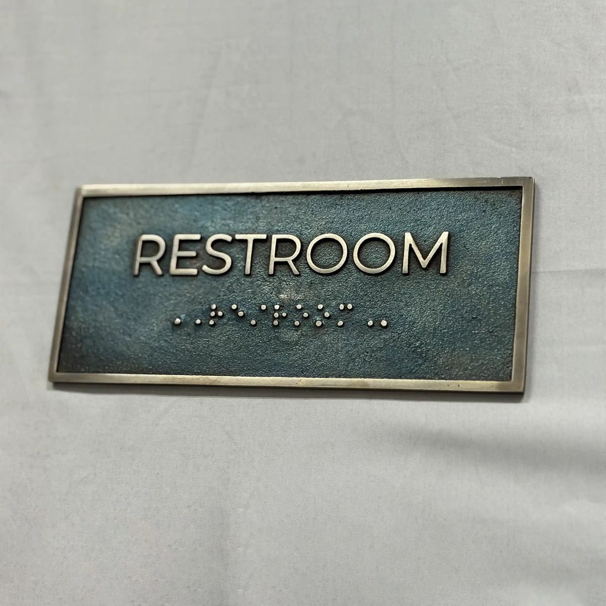 Rectangular sign with 'RESTROOM' text and braille on a gray background