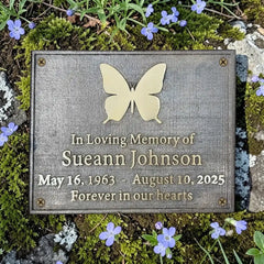 Memorial plaque with butterfly design and engraved text on a natural background with flowers.