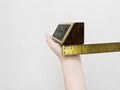 Hand holding a gold bar with a ruler for scale on a light gray background