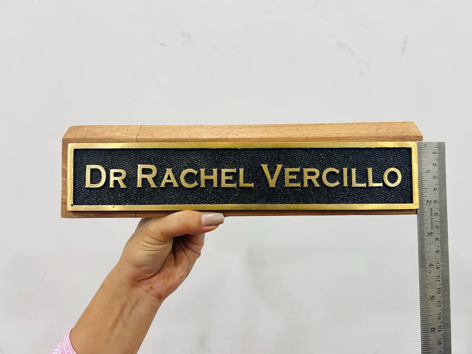 Hand holding a nameplate with 'DR Rachel Vercillo' and a ruler for scale on a light gray background