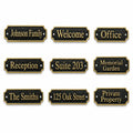 Nine personalized house nameplate options shown on a plain white background, each with a black textured face, gold border, and gold lettering for phrases such as Johnson Family, Welcome, Office, Reception, Suite 203, Memorial Garden, The Smiths, 125 Oak Street, and Private Property.